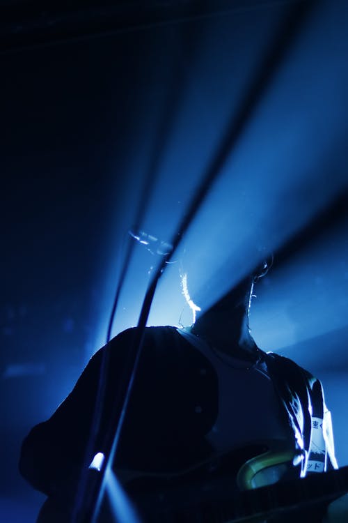 Anonymous male guitarist singing into microphone while playing guitar during live performance in blue light rays
