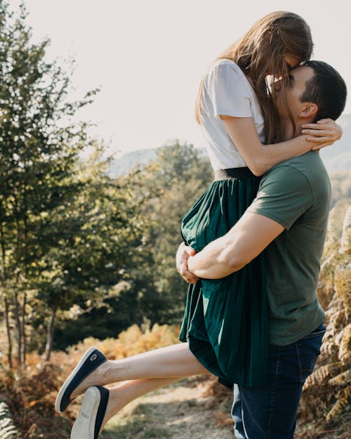 Side view of loving couple in casual clothes hugging and looking at each other while standing in countryside