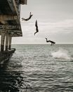 Multiple exposure of men in swimwear jumping from pier into calm water of sea in cloudy day