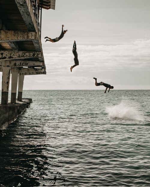 Free Multiple exposure of men in swimwear jumping from pier into calm water of sea in cloudy day Stock Photo