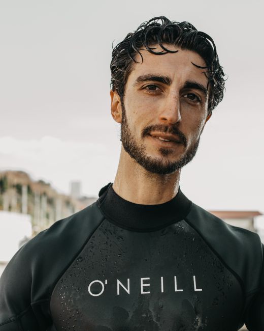 Pensive ethnic male with beard and dark hair in wetsuit standing on street in daytime