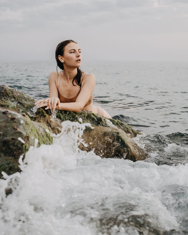 Female Leaning On Rocks While Swimming In Wavy Sea