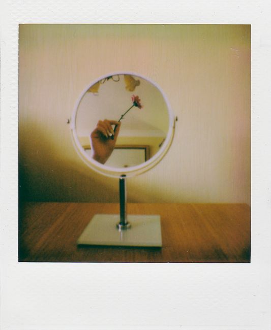 A creative reflection of a hand holding a flower in a mirror on a wooden table.