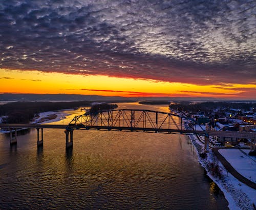 A Silhouette of a Bridge Above a River During Sunset