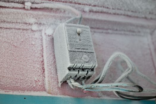 An electrical switch covered in frost and ice during winter on a building's exterior wall.