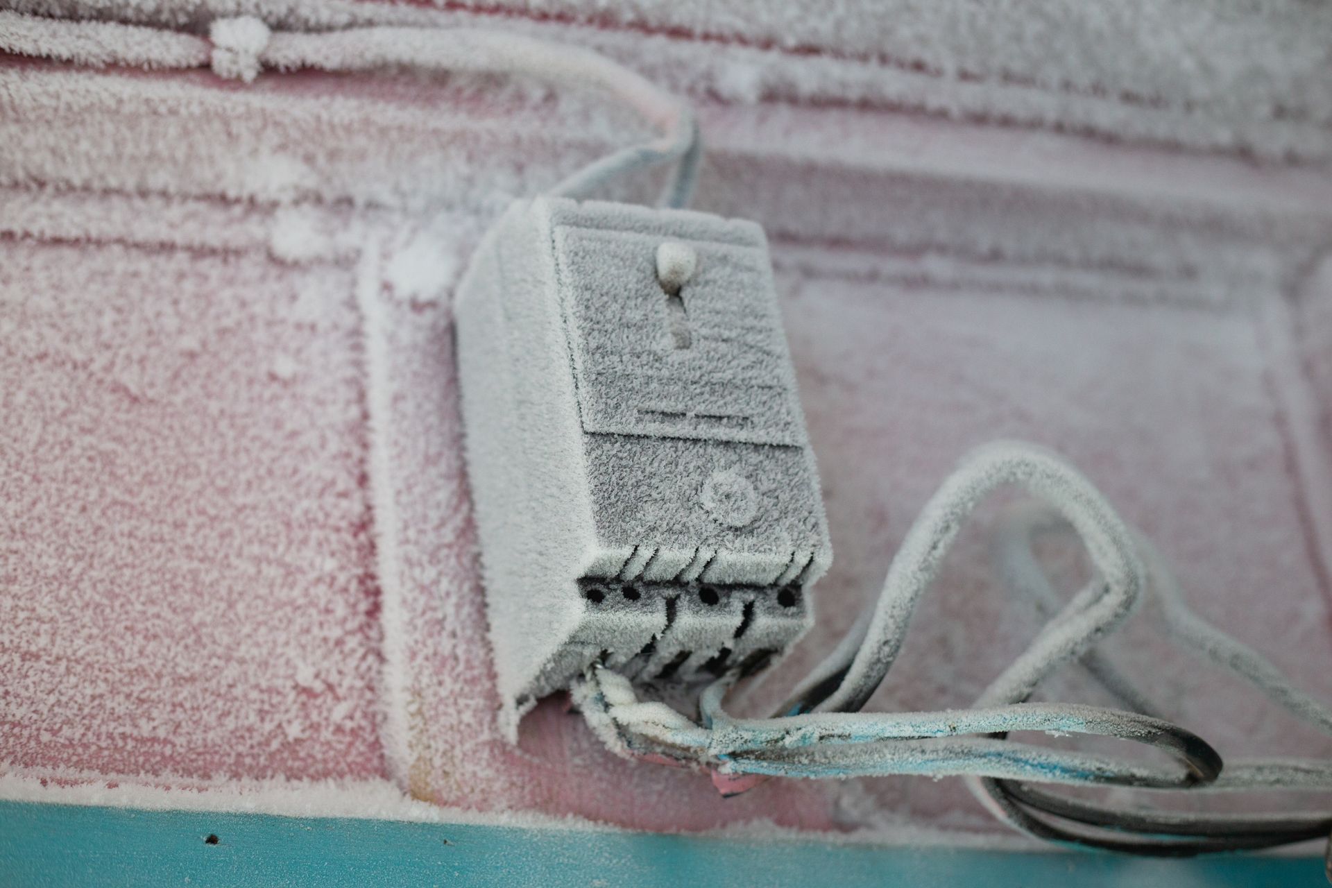 An electrical switch covered in frost and ice during winter on a building's exterior wall.
