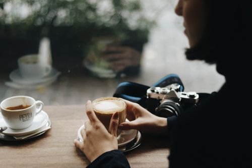 Free Side view of crop anonymous female with delicious coffee and vintage photo camera at cafeteria table Stock Photo