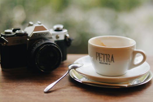 A stylish vintage camera beside a coffee cup in a cozy café setting.