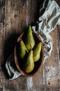 Bowl with ripe green pears and cotton napkin placed on lumber rustic table