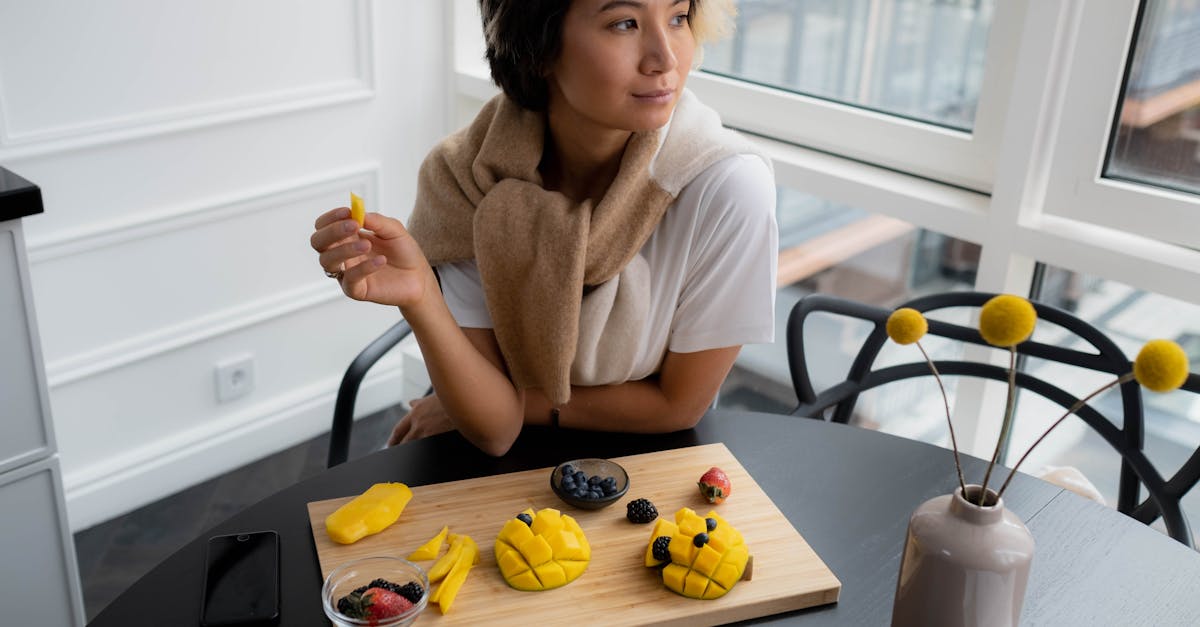 Asian woman savoring sliced mango and berries on a wooden board in a cozy indoor setting. Asian woman savoring sliced mango and berries on a wooden board in a cozy indoor setting.