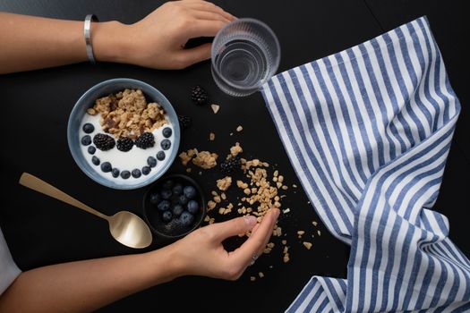 Delicious flat lay breakfast setup with granola, berries, and yogurt on a sleek black surface, perfect for a fresh morning meal.