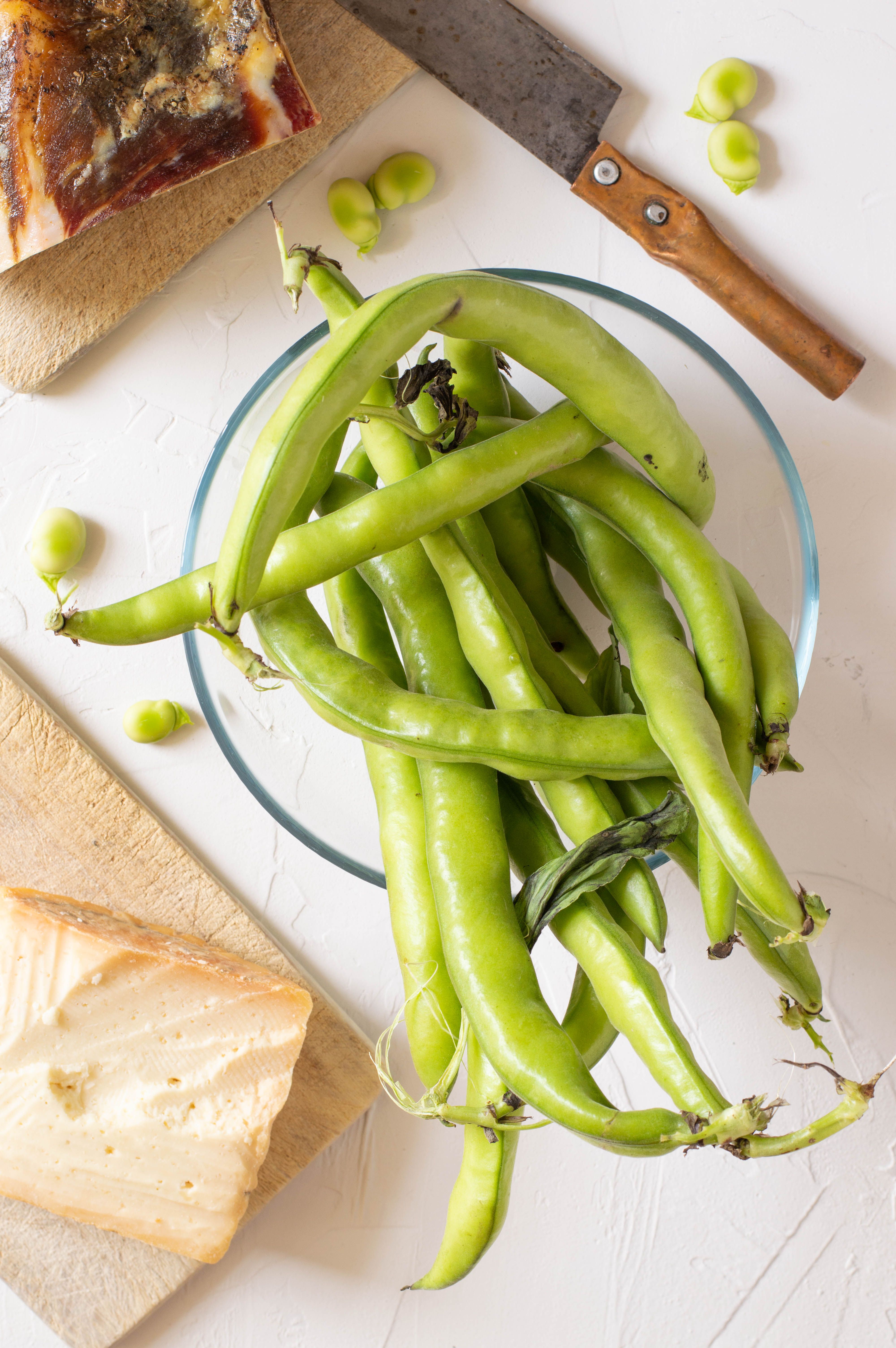A close-up of fresh green beans with cheese and meat slices on a cutting board.