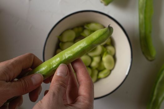 Hands peeling fresh broad beans into a bowl, capturing the freshness and richness of nutritious food.