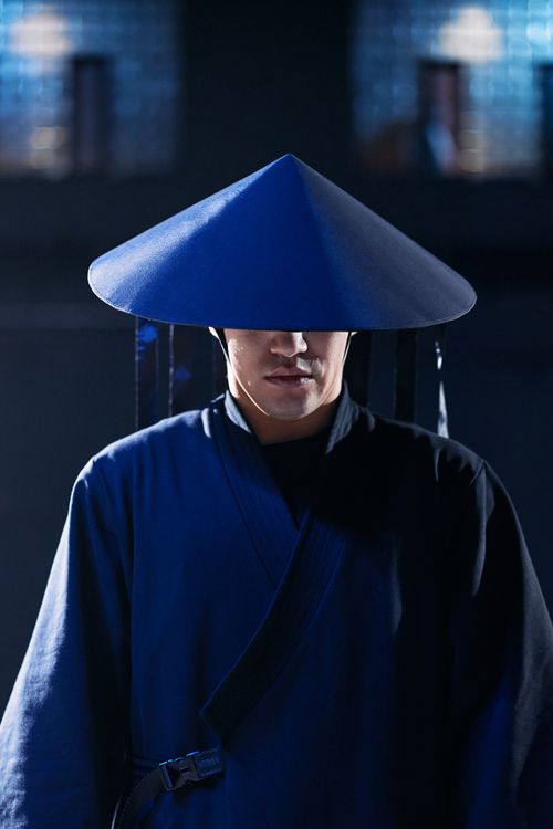Free A man dressed in a blue ninja costume with a conical hat, in a low-light setting. Stock Photo