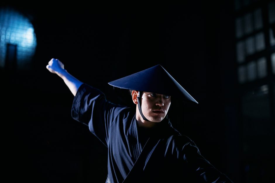 A dynamic studio portrait of a man in traditional costume and hat performing a dramatic pose.