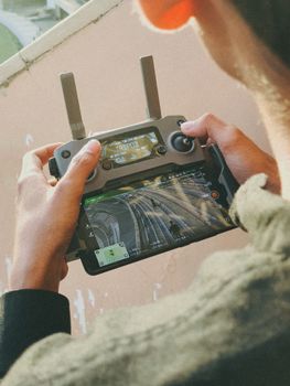 Hands operating a drone controller, displaying aerial view on screen, outdoors in Ranchi, India.