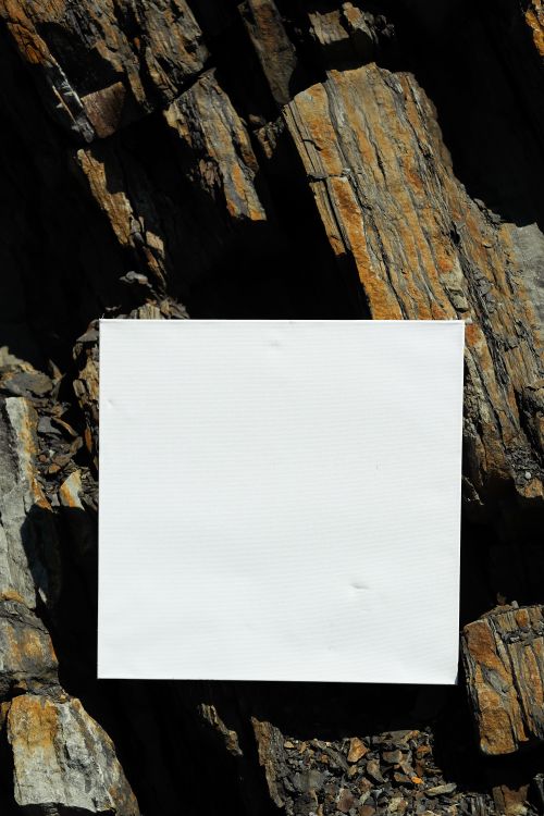 Free A blank white paper set against a textured rock surface, ideal for text placement or mockups. Stock Photo