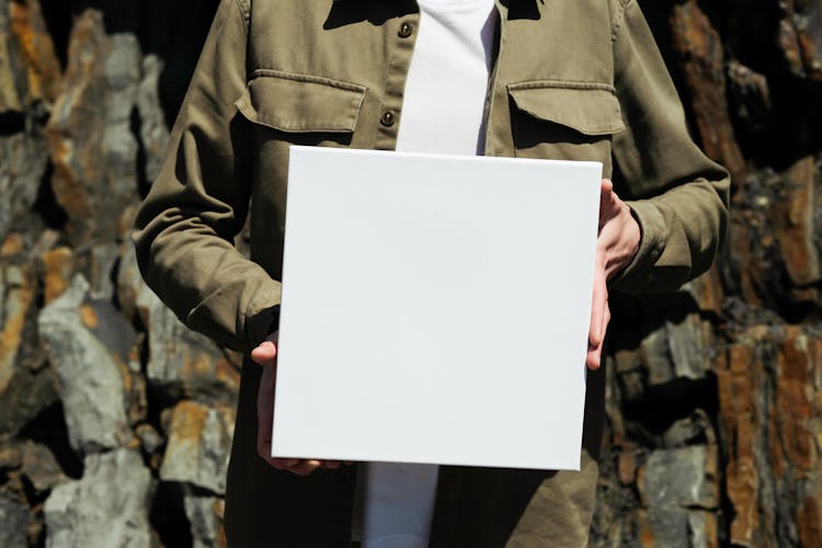 Person In Khaki Jacket Holding White Square Box