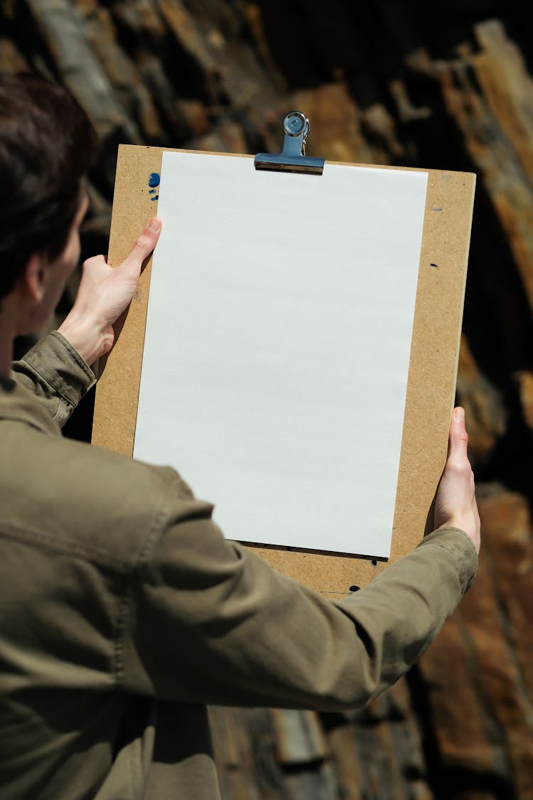 A Person Holding A Clipboard With White Paper