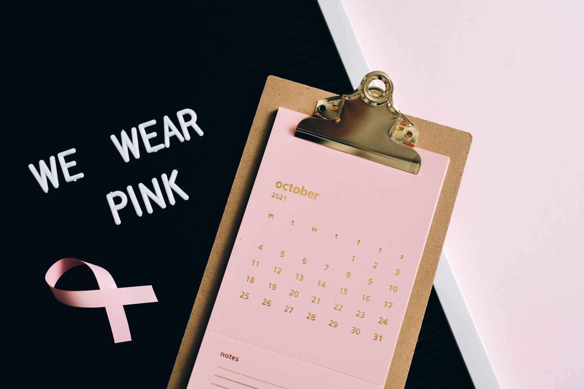 Flat lay image of calendar and pink ribbon for breast cancer awareness in October.