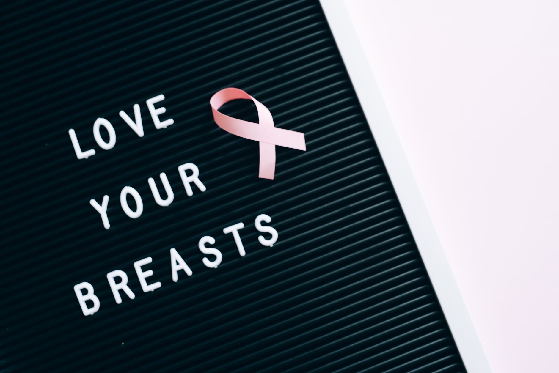 Pink ribbon and inspirational message "Love Your Breasts" on letter board for breast cancer awareness.