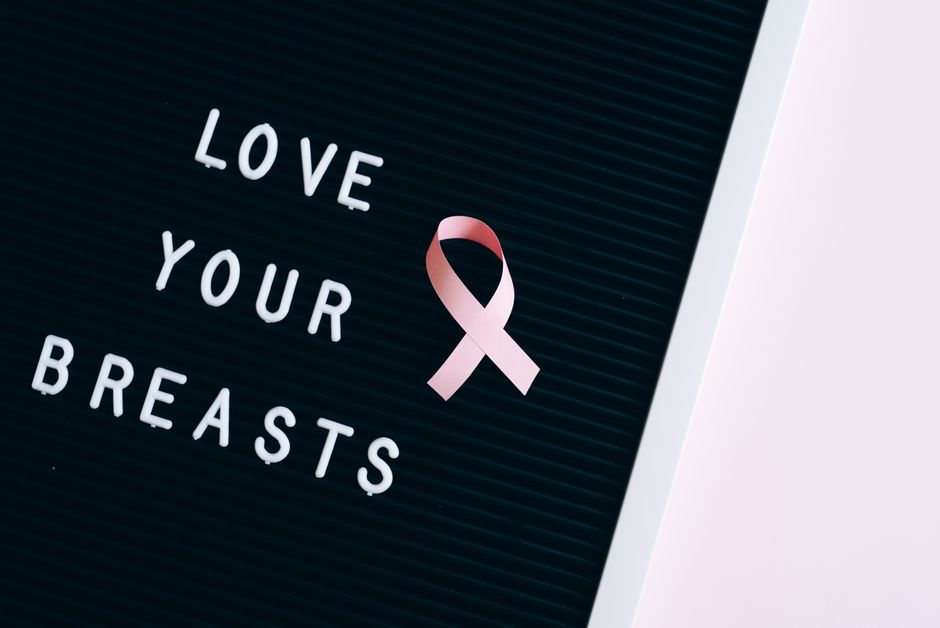 Close-up of a letter board with 'Love Your Breasts' and a pink ribbon symbolizing breast cancer awareness.