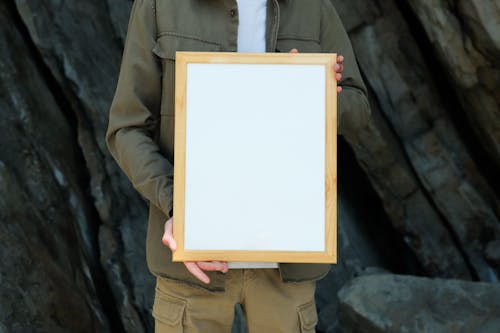 A Person Wearing Green Jacket Holding a Blank Wooden Frame