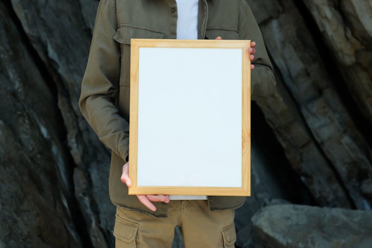 A Person Wearing Green Jacket Holding A Blank Wooden Frame