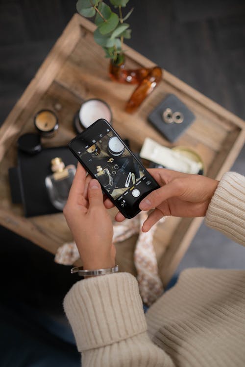Person Taking Photo of Perfume and Accessories on a Wooden Tray