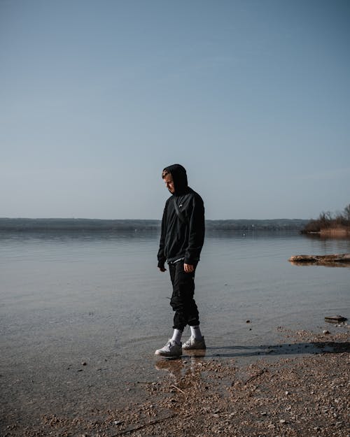 A Man in Black Hoodie Walking on the Shore