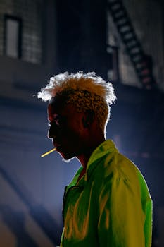 Profile view of a man wearing a neon jacket with a lollipop in an industrial setting.