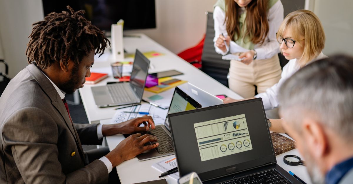 Equipo diverso de profesionales colaborando con laptops en una oficina moderna, simbolizando la transformación digital empresarial.
