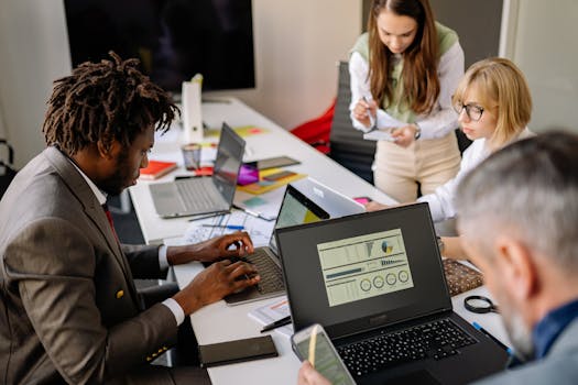 Diverse coworkers engaged in teamwork using laptops and digital devices in a modern office setting.