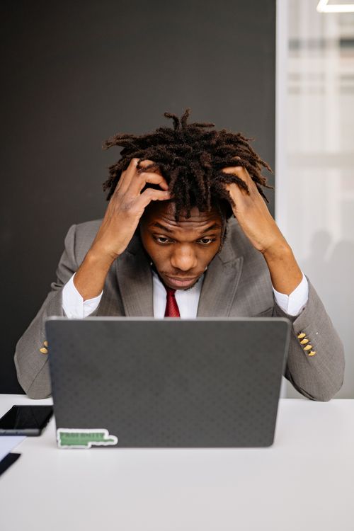 Exhausted man at laptop with head in hands — burnout's three dimensions of exhaustion, cynicism, and reduced efficacy often look indistinguishable from depression