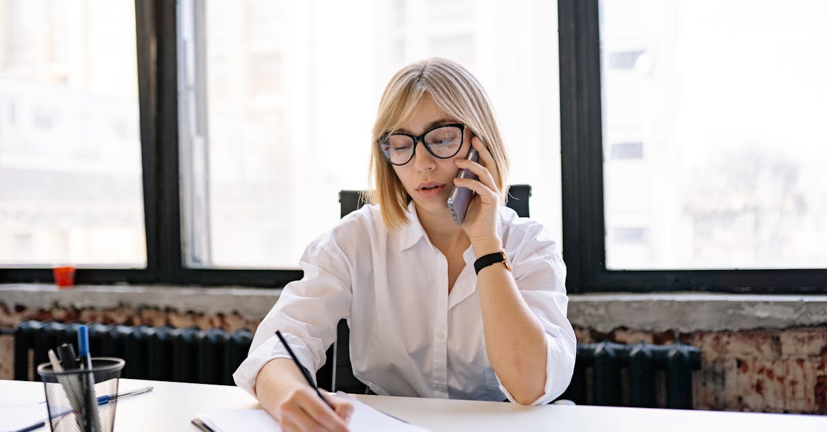 A woman in an office setting multitasking with a phone call and taking notes.