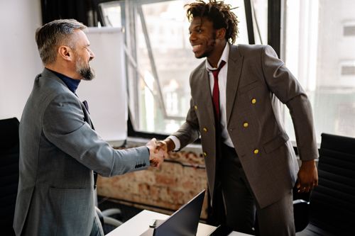 Free Two businessmen shaking hands and smiling in a modern office setting, sealing a successful deal. Stock Photo