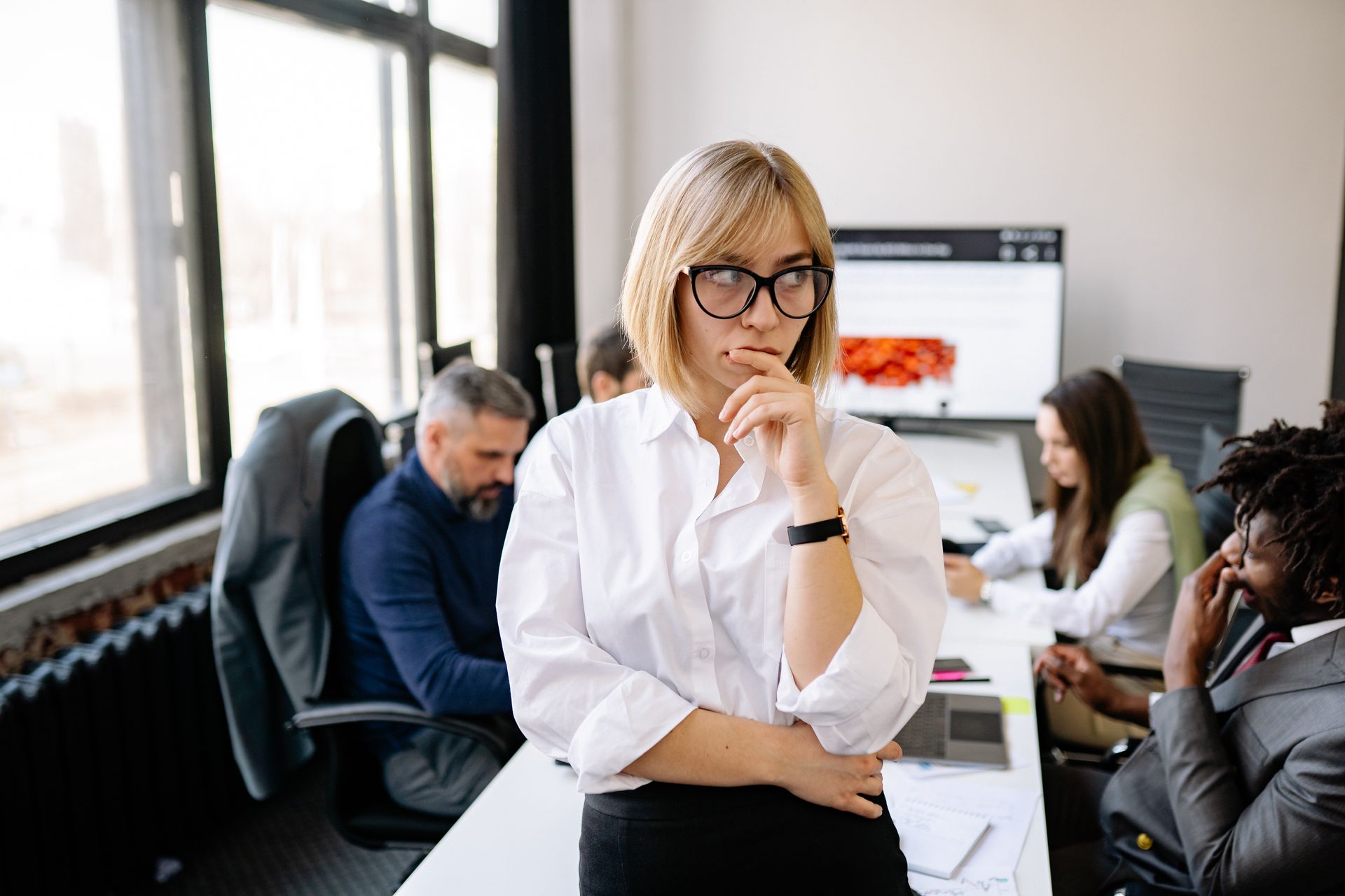 A focused businesswoman thinking during a team meeting in a modern office.