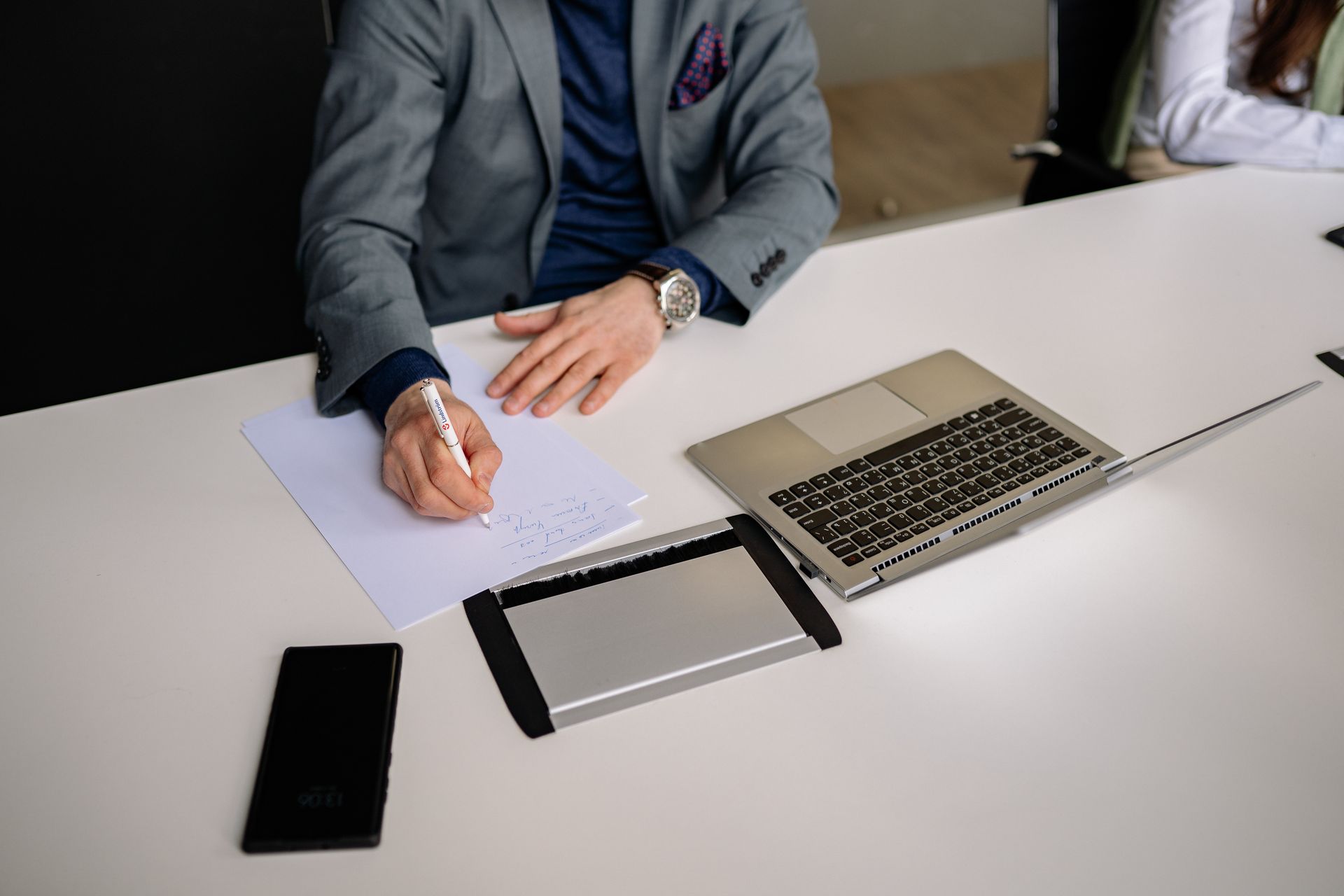Professional businessman writing notes in a modern office environment with laptop and smartphone.