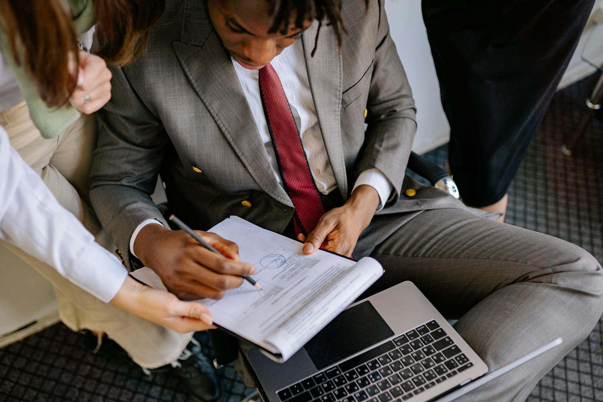 A businessman in a suit signing a contract with colleagues' assistance.