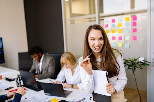 Smiling businesswoman in corporate office with colleagues working in the background.