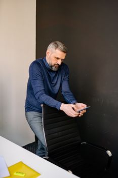 Middle-aged man in blue sweater checking his phone in a modern office setting.