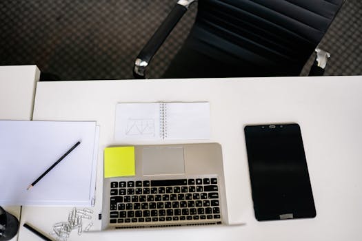 Top view of a tidy office desk with laptop, tablet, and stationery.