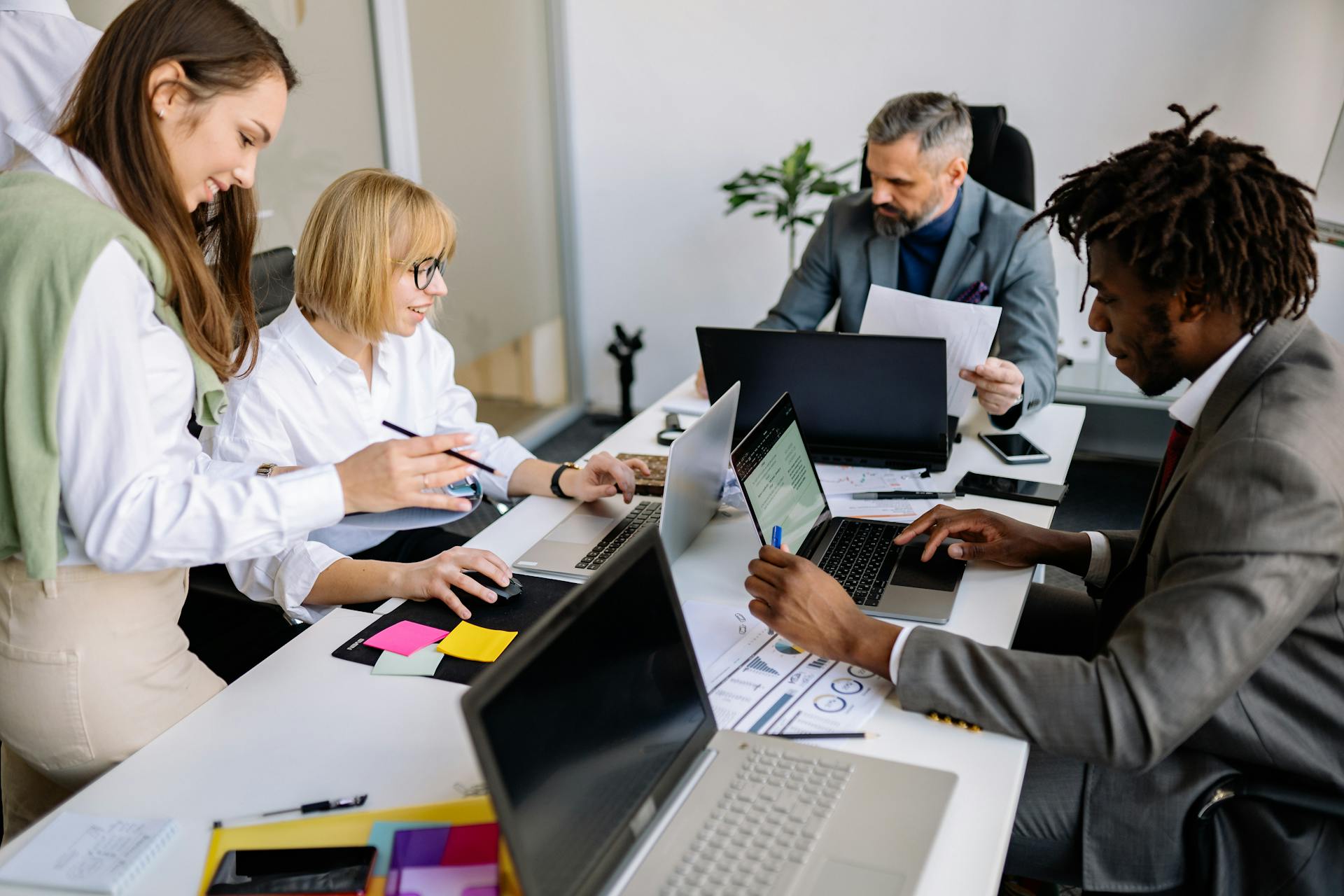 A diverse team collaborates in a modern office setting with laptops and documents.