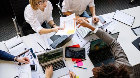 Diverse team collaborating in a modern office with laptops and documents.