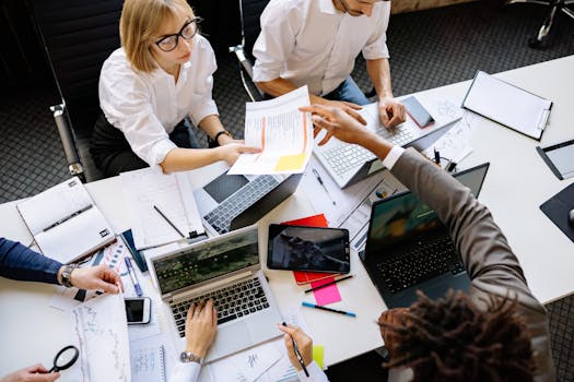 Diverse team collaborating in a modern office with laptops and documents.