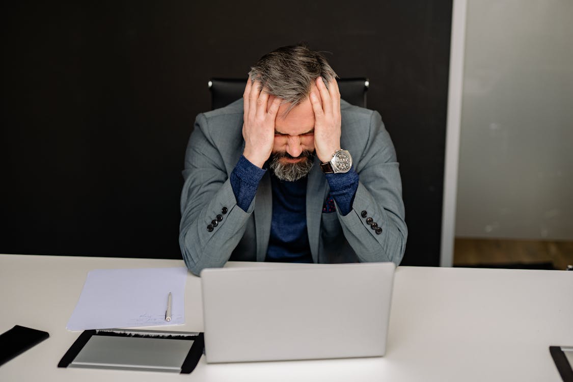 Man in Gray Suit Jacket Covering His Face With His Hand, stressed before delegating tasks