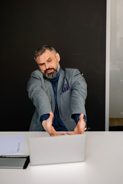 Free Stressed businessman expressing frustration while sitting at a desk with a laptop in an office setting. Stock Photo