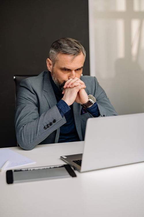 Free Businessman deep in thought while looking at laptop, hands clasped at office desk. Stock Photo