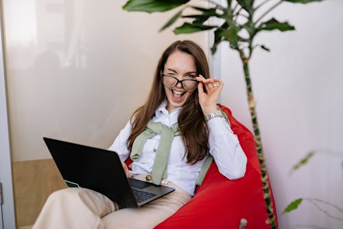 Free A Woman Sitting on a Bean Bag Using a Laptop Stock Photo