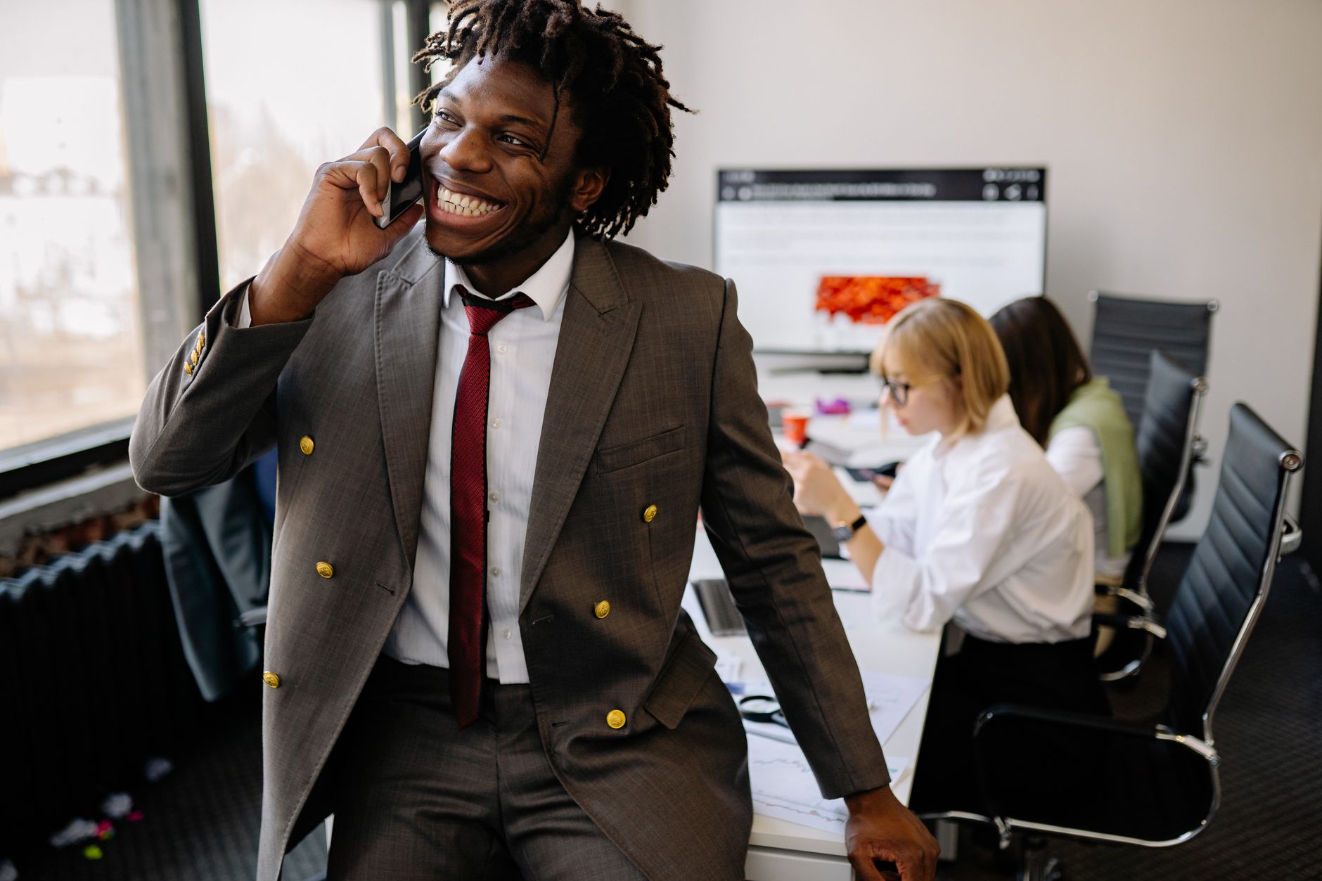 Confident businessman with dreadlocks smiling while on a phone call in a modern office setting.